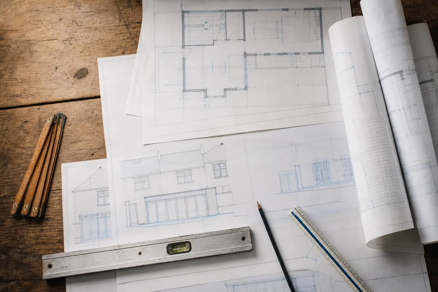 Architectural drawings for a house extension laid out on a workbench with a folding rule and spirit level